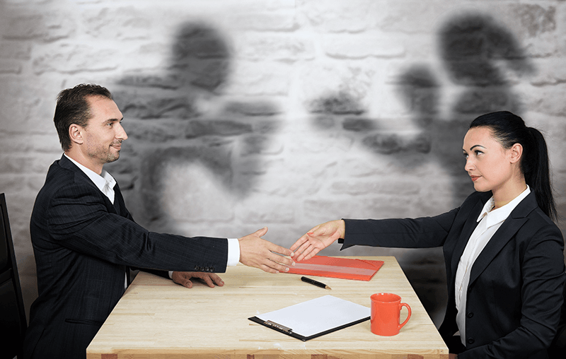 A man and woman shaking hands at a desk, questioning if their communication style is hindering them.
