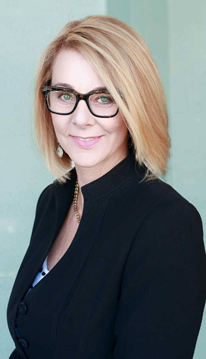A woman with shoulder-length blonde hair and black-rimmed glasses, who is known as a Growth Architect, is wearing a black blazer and smiling at the camera.