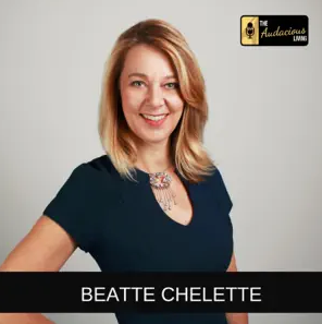 A person with shoulder-length blonde hair wearing a blue shirt stands smiling. A logo in the top right corner reads "The Audacious Living." Text at the bottom reads "Beatte Chelette from Beate Chelette Media.