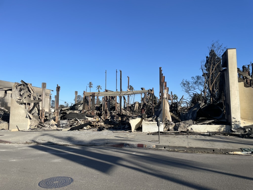 Amid the charred debris and skeletal structural beams of the building, a clear blue sky serves as a hopeful reminder to do better in 2025.