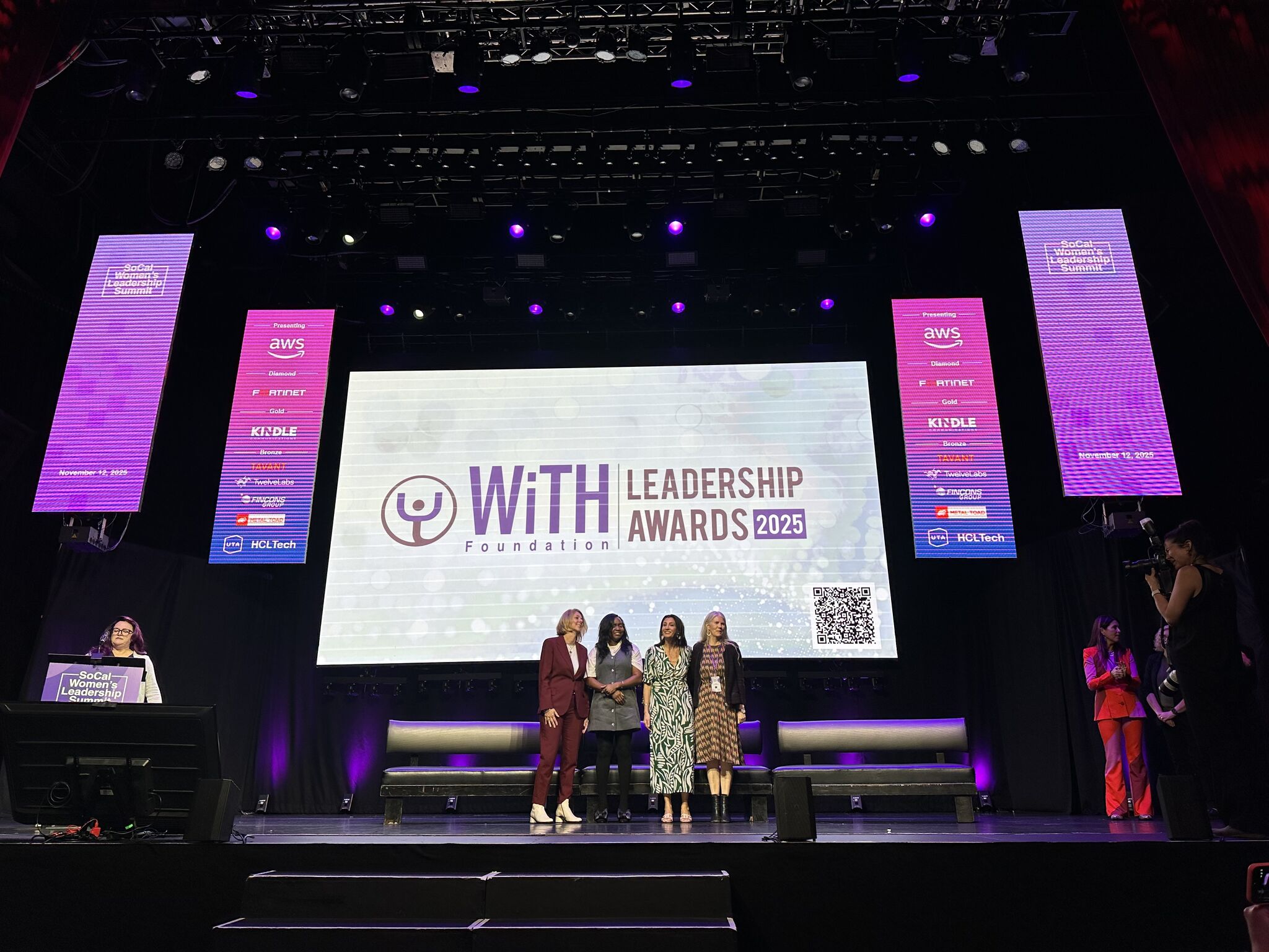 Four women stand on stage at the WiTH Foundation Leadership Awards 2025 event, where "AI Is Rising — How It Can Help You as a Small Business Owner" is highlighted on a large screen with a QR code in the background.
