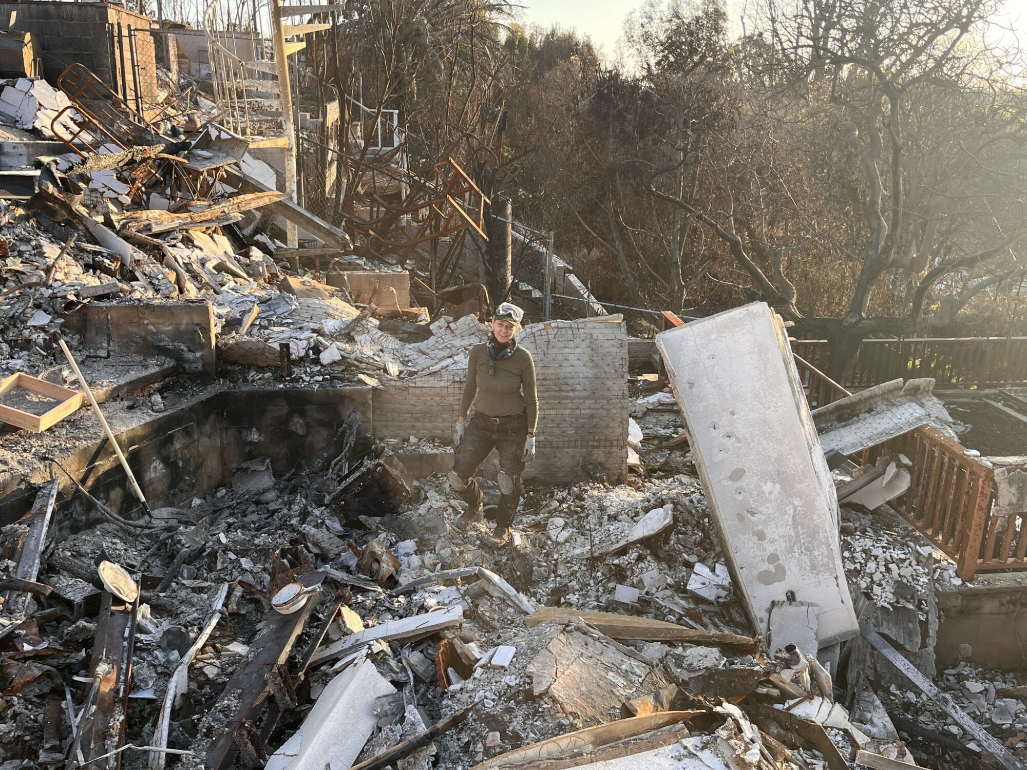 A person stands amid the charred remains and debris of a burned-down building, surrounded by ash—reminding us that even after loss, AI Is Rising — How It Can Help You as a Small Business Ow to rebuild and recover stronger.