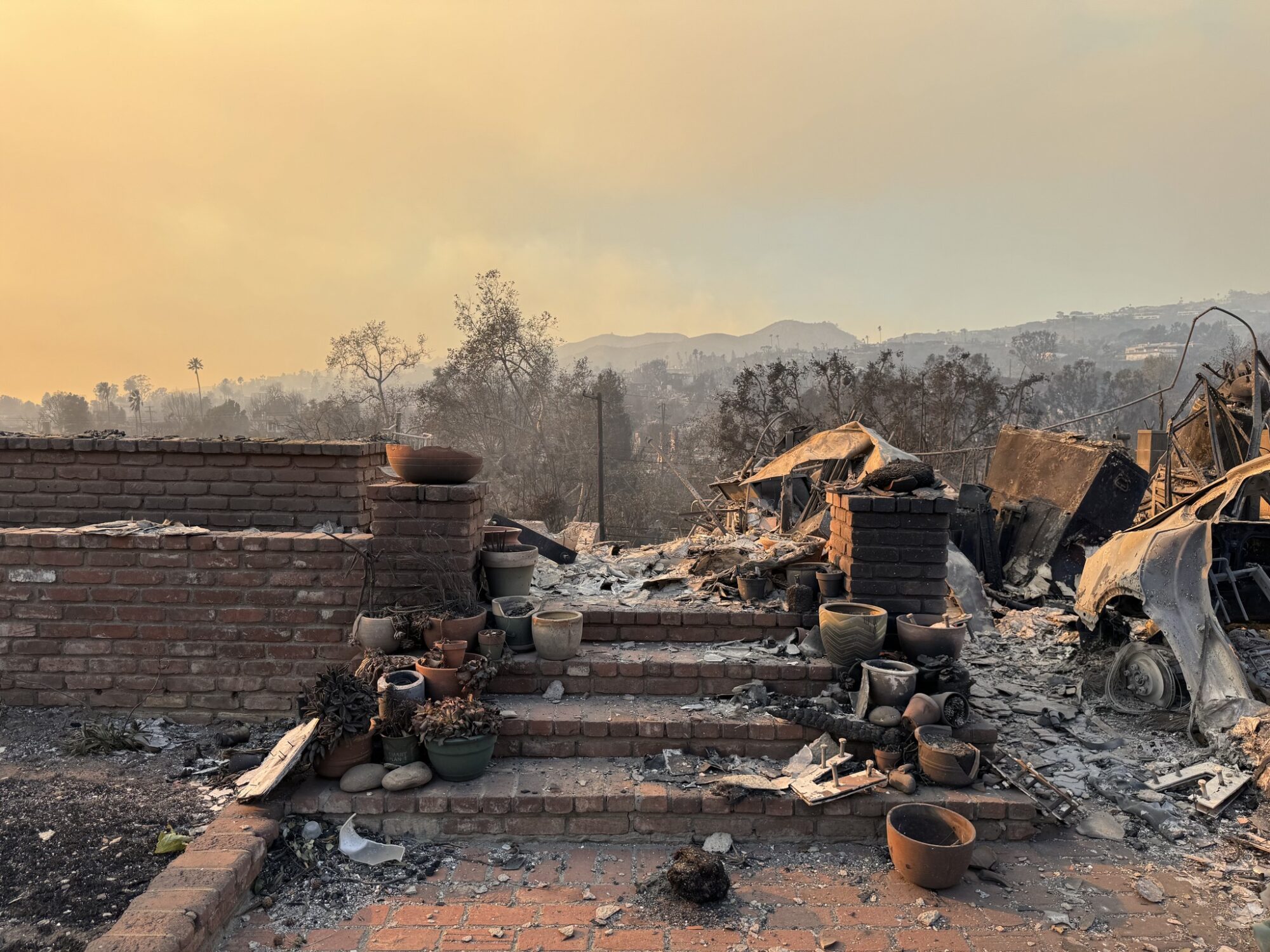 Burned remains of a house, with scorched bricks, broken pots, and ash-covered debris against a smoky sky and hills—a stark reminder of resilience and recovery, much like how AI is rising to help you as a small business owner rebuild after setbacks.